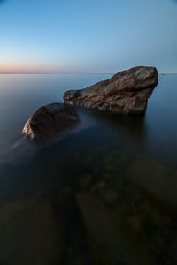 Scenic view of rocks by sea against clear sky