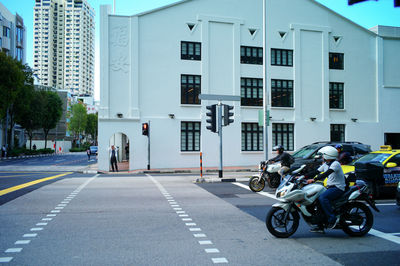 People riding motorcycle on road against buildings in city