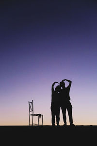 Silhouette couple making heart shape while standing against sky at dusk