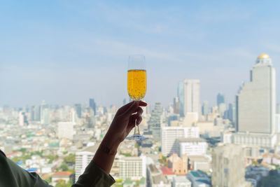 Midsection of man holding glass against buildings in city