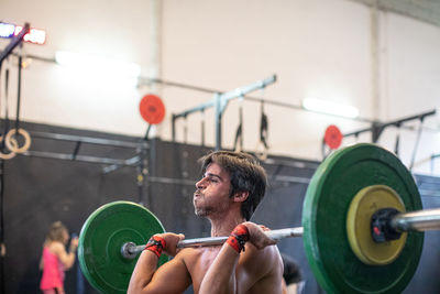 Muscular guy lifting barbell in modern gym