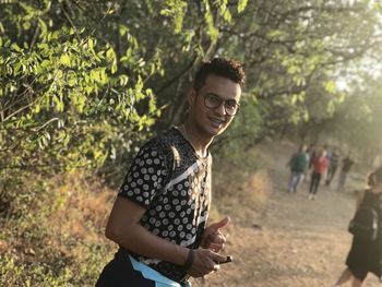 Smiling young man standing against trees