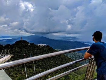 Rear view of man standing on railing against sky