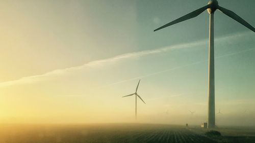 Low angle view of wind turbines on field against sky