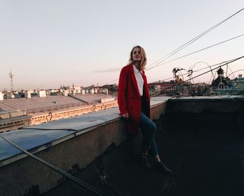 Portrait of woman leaning on retaining wall at building terrace against sky