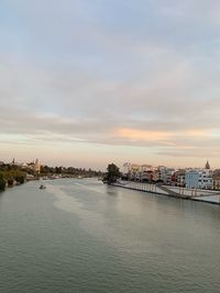 Scenic view of river by buildings against sky during sunset