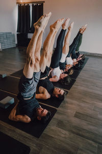 From above of group of adult sporty people in sportswear with legs raised stretching body in salamba sarvangasana pose on sports mats while practicing yoga in modern studio