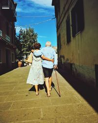 Rear view of senior couple walking on street amidst buildings