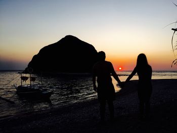 Silhouette of couple holding hands against sea during sunset