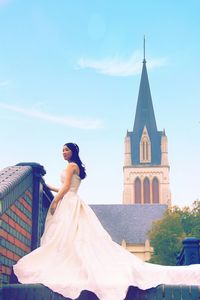 Beautiful bride standing by church against sky