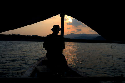 Silhouette men on boat against sky during sunset