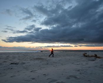 Man running on beach against sky during sunset