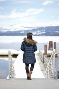 Rear view of woman wearing warm clothing standing on pier over sea