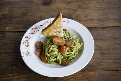 High angle view of bread slice garnished on spaghetti pasta served in bowl on table