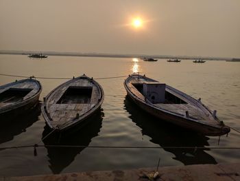 Boats moored in lake against sky during sunset