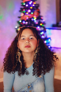 Portrait of young woman against illuminated christmas tree at home