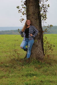 Portrait of smiling teenage girl standing by tree trunk at field