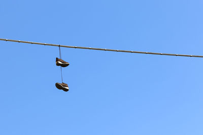 Low angle view of shoes hanging from cable against sky
