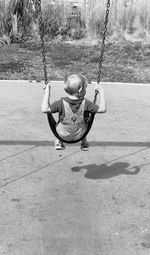 Rear view of boy swinging at playground during sunny day