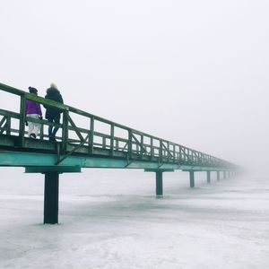 Low angle view of people walking on bridge over frozen river during foggy weather