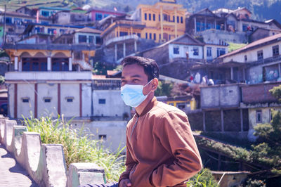 Portrait of young man wearing mask standing against traveling in city