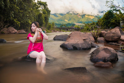 Young woman sitting on rock against water