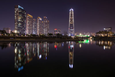Illuminated buildings by river against sky at night