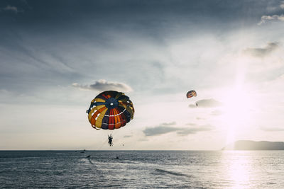 People paragliding over sea against sky during sunset