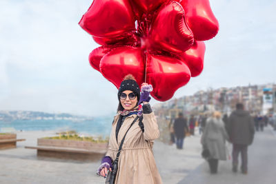 Portrait of woman with red balloons standing against sky