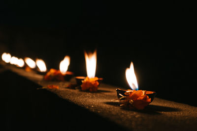 Close-up of diyas with flowers on retaining wall at night