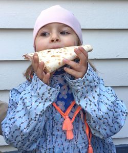 Cute girl eating food against wall