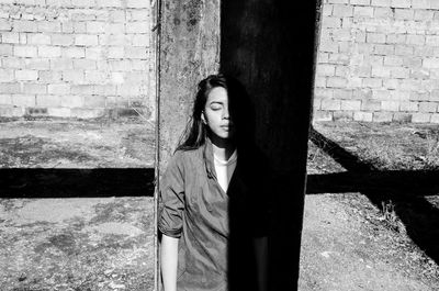 Portrait of young woman standing against brick wall