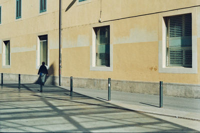Rear view of person walking on sidewalk against building