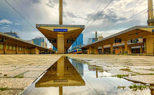 Reflection of bridge in puddle on city street against sky