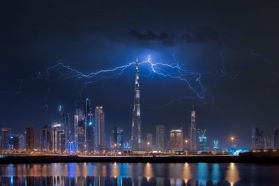 Reflection of illuminated buildings in lake against lightning