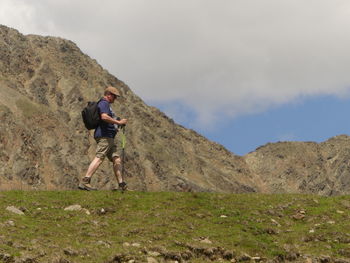 Side view full length of male hiker walking by mountain on field