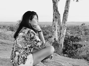 Portrait of young woman sitting on tree against sky