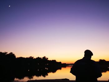 Silhouette man looking at lake against sky during sunset