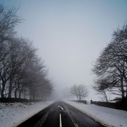 Empty road amidst snow covered trees against sky