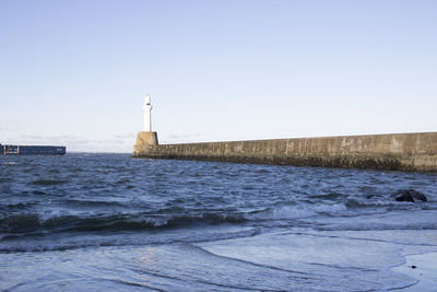 Lighthouse by sea against clear sky