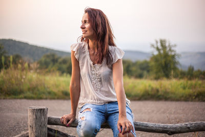 Woman sitting on railing against sky during sunset