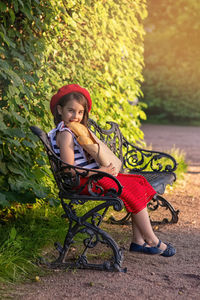 Beautiful brunette girl sits on a bench, holding a french baguettes