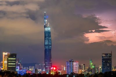 Illuminated buildings in city against cloudy sky