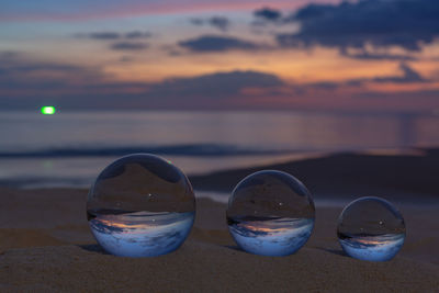 Close-up of glasses on beach against sky during sunset