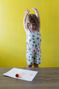 Cute girl with arms raised looking at paper on table