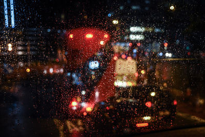 Illuminated city seen through wet window during rainy season