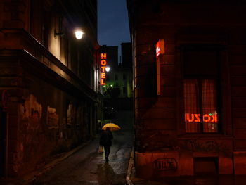 Man with yellow umbrella walking on illuminated street at night