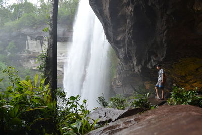 Rear view of man standing on rock against waterfall