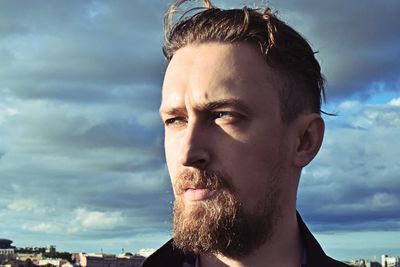 Bearded man looking away against cloudy sky