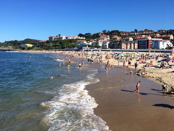 People at beach against clear blue sky